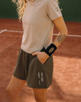 Woman wearing Cuera Womens Active Globe Shorts in Army, lifestyle action shot on the padel court