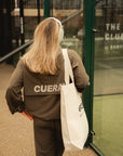 Model wearing Cuera Active Cuera Track Jacket in Army, lifestyle action shot on the padel court