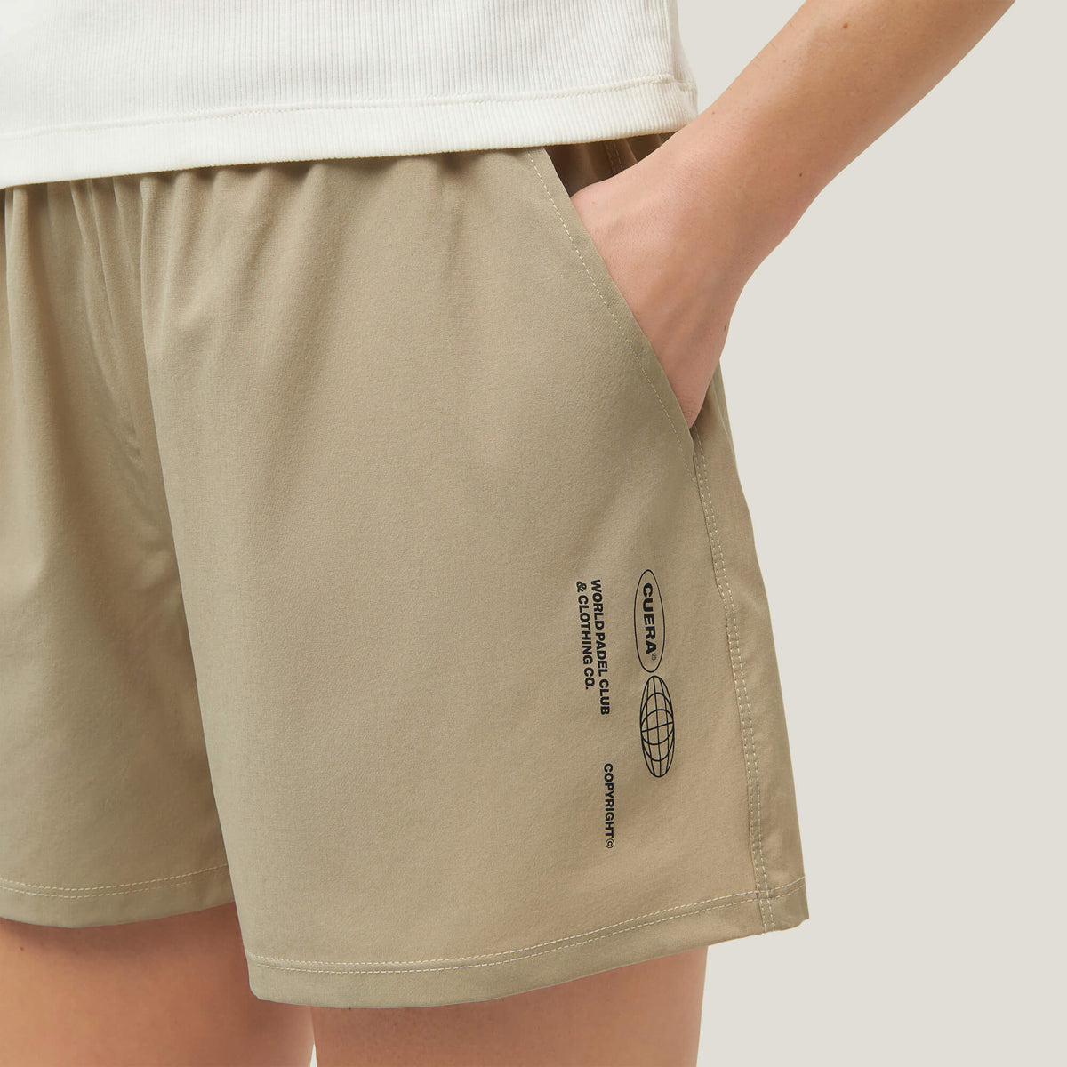 Woman wearing Cuera Womens Active Globe Shorts in Sand, close-up detail on model
