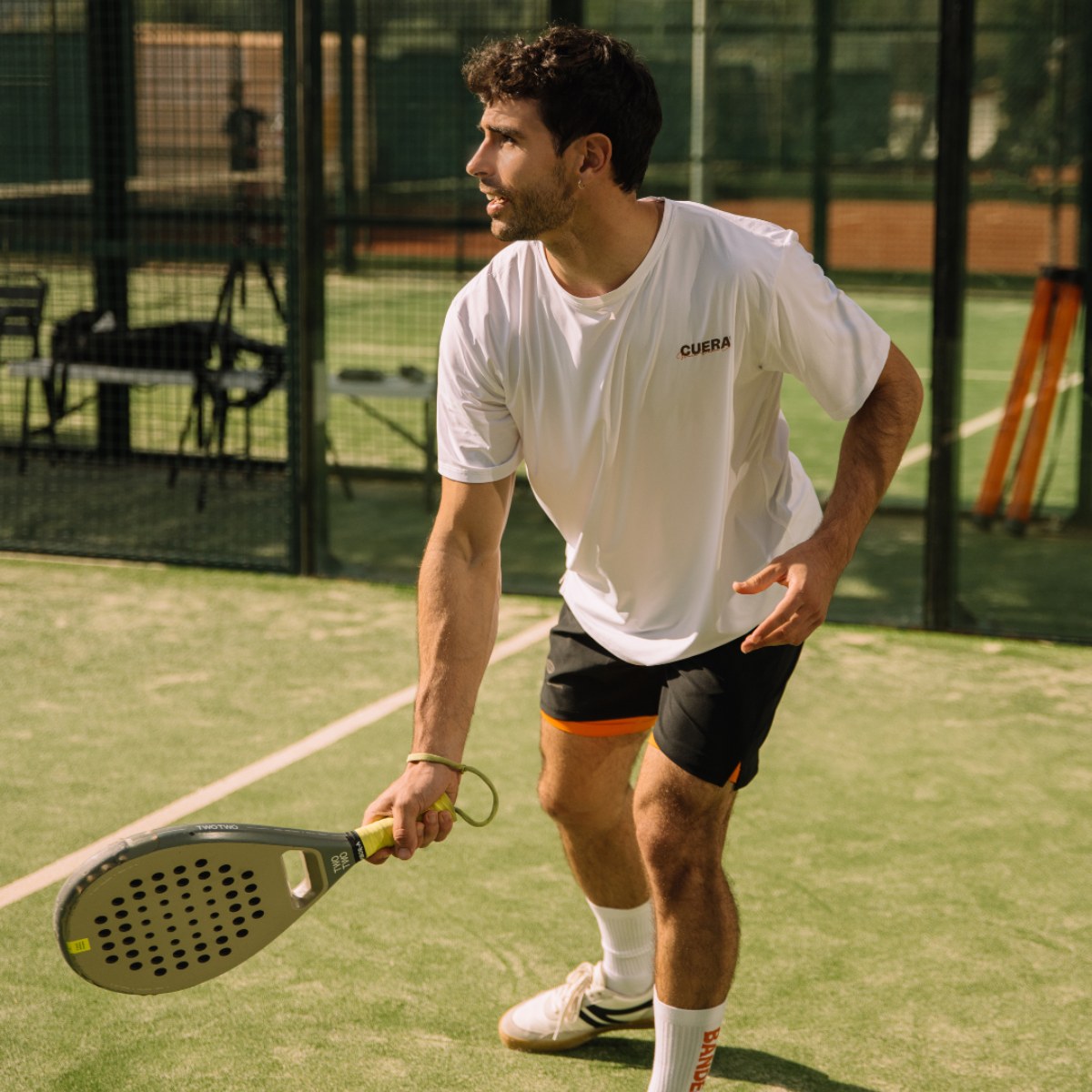 Model wearing Cuera Active Light Weight T-Shirt in White w. walnut, lifestyle action shot on the padel court