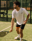 Model wearing Cuera Active Light Weight T-Shirt in White w. walnut, lifestyle action shot on the padel court