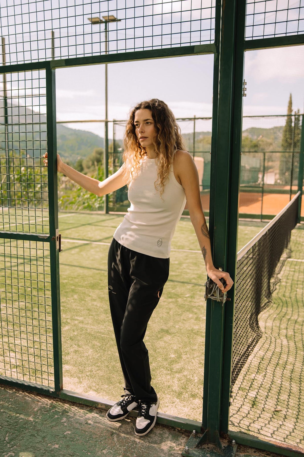Model wearing Cuera Active Rib Tank Top in Off White, lifestyle action shot on the padel court