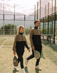 Model wearing Cuera Active Track Jacket in Black / Walnut, lifestyle action shot on the padel court