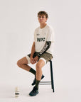 Model wearing Cuera Active WPC Light Weight T-Shirt in Off White / Army, lifestyle action shot on the padel court