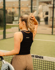 Model wearing Cuera Oncourt Cropped Tank Top in Black, lifestyle action shot on the padel court