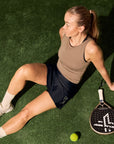 Model wearing Cuera Oncourt Cropped Tank Top in Walnut, lifestyle action shot on the padel court