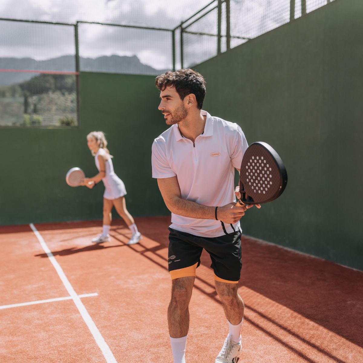 Model wearing Cuera Oncourt Made Polo ss in White, lifestyle action shot on the padel court